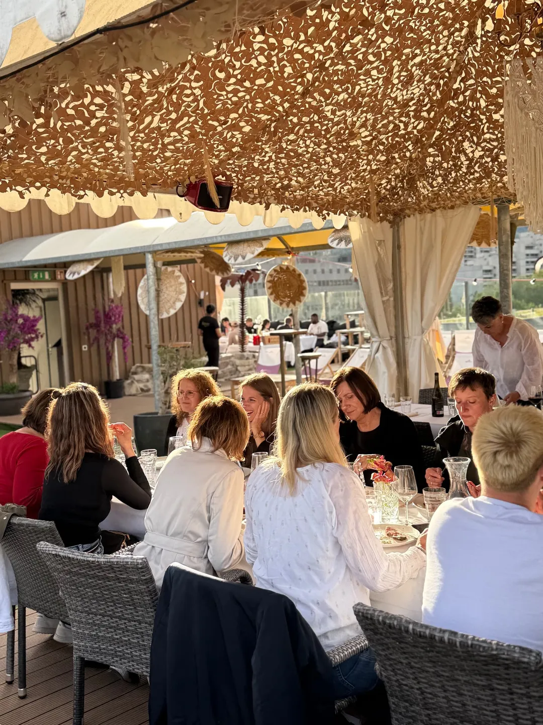 Gäste beim gemeinsamen Essen unter dem Sonnensegel auf der Rooftop Aarau Terrasse