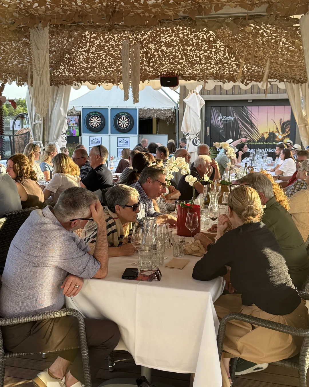 Gäste an langen Tafeln unter dem Sonnensegel bei einem Event im Rooftop Aarau