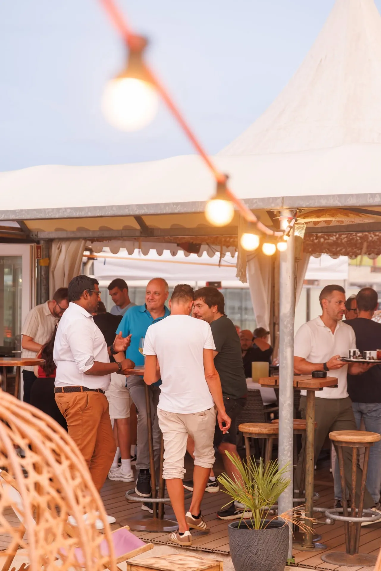Gäste beim Apéro an Stehtischen unter dem Pavillon mit Lichterketten im Rooftop Aarau